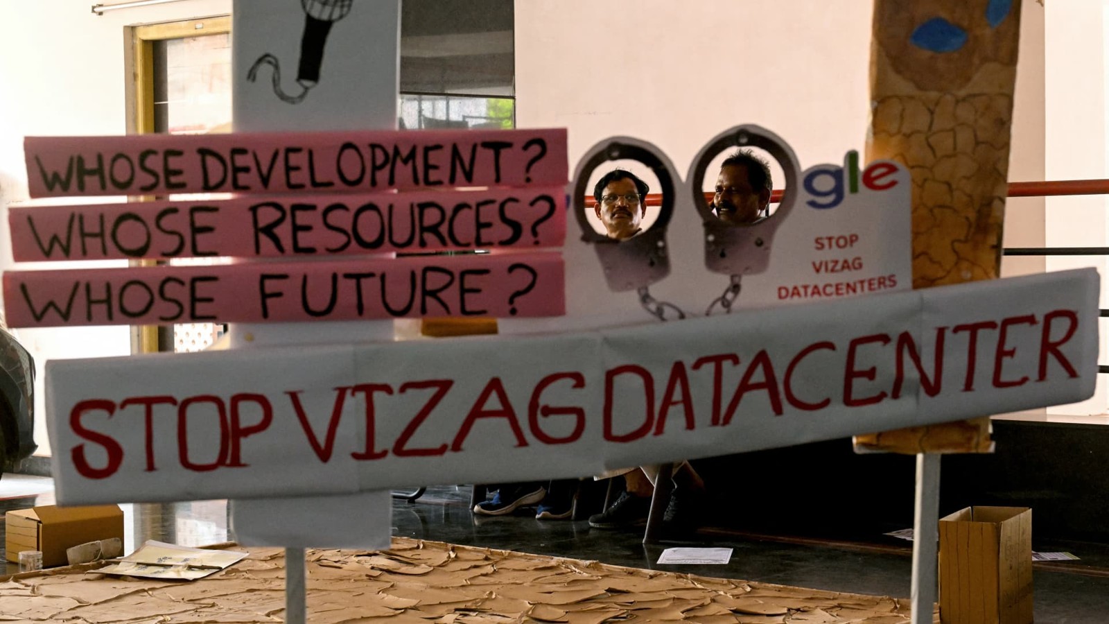 Men sit behind a display opposing a Google AI and data-center hub at an event in Visakhapatnam, September 6, 2026.