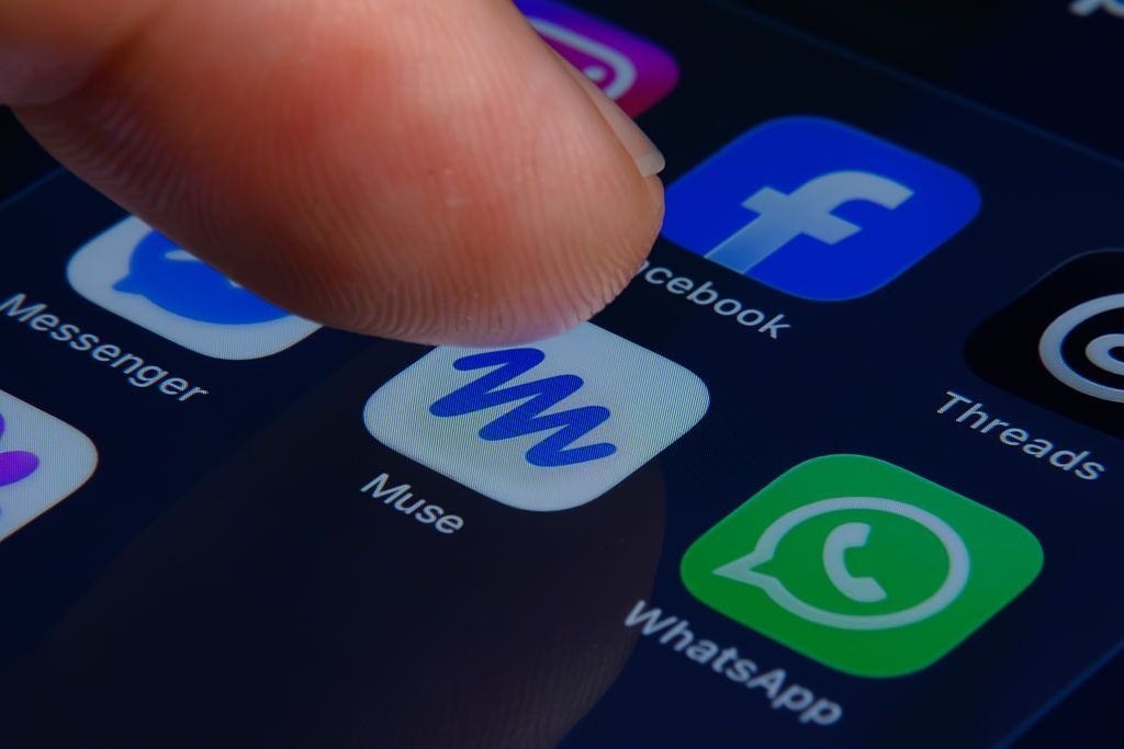 A finger points to the Muse app icon on a smartphone. The photograph does not demonstrate the company’s user or revenue claims.