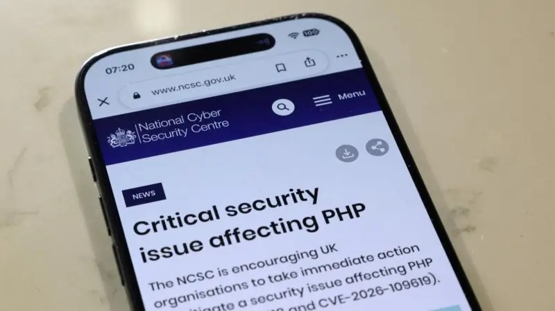 A phone displays the UK National Cyber Security Centre warning about a critical PHP security issue.